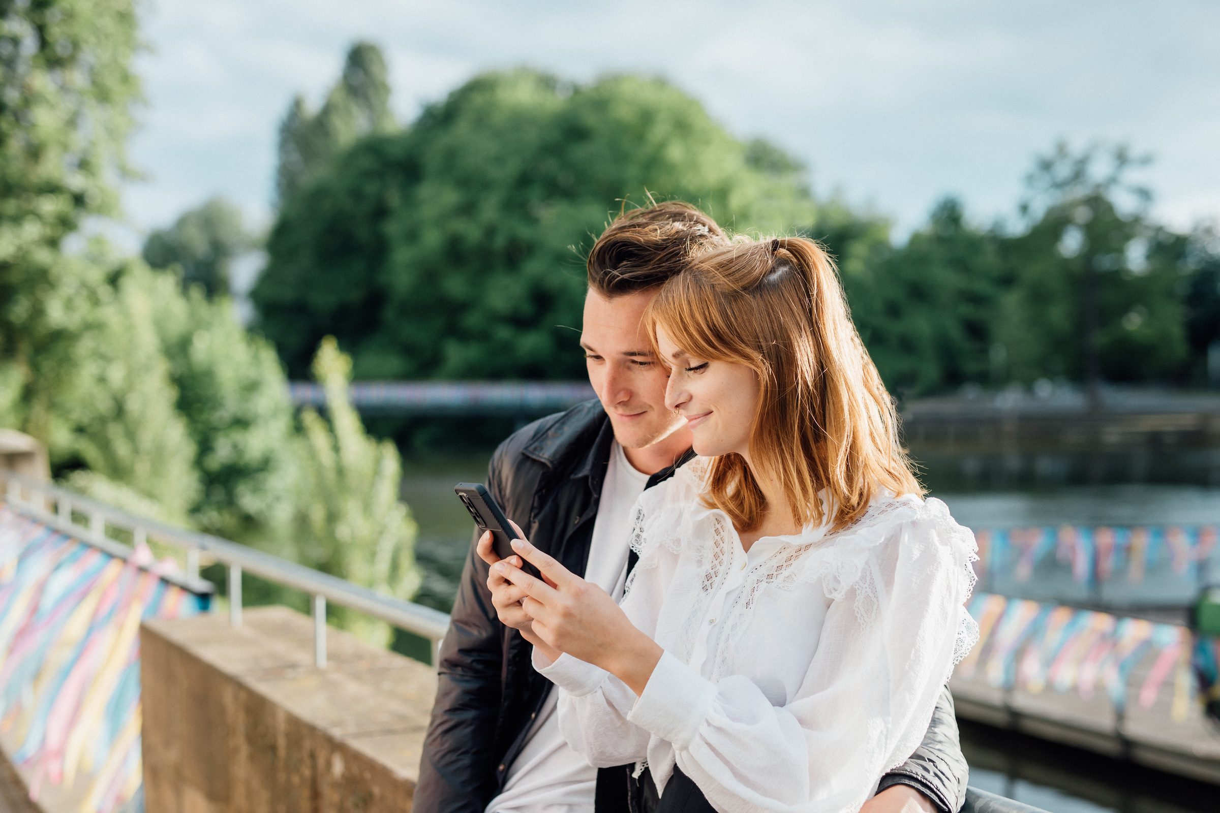 Junges Paar lehnt an einem Geländer am Fluss und schaut gemeinsam auf ein Smartphone, Kampagne der Stadtwerke Heilbronn