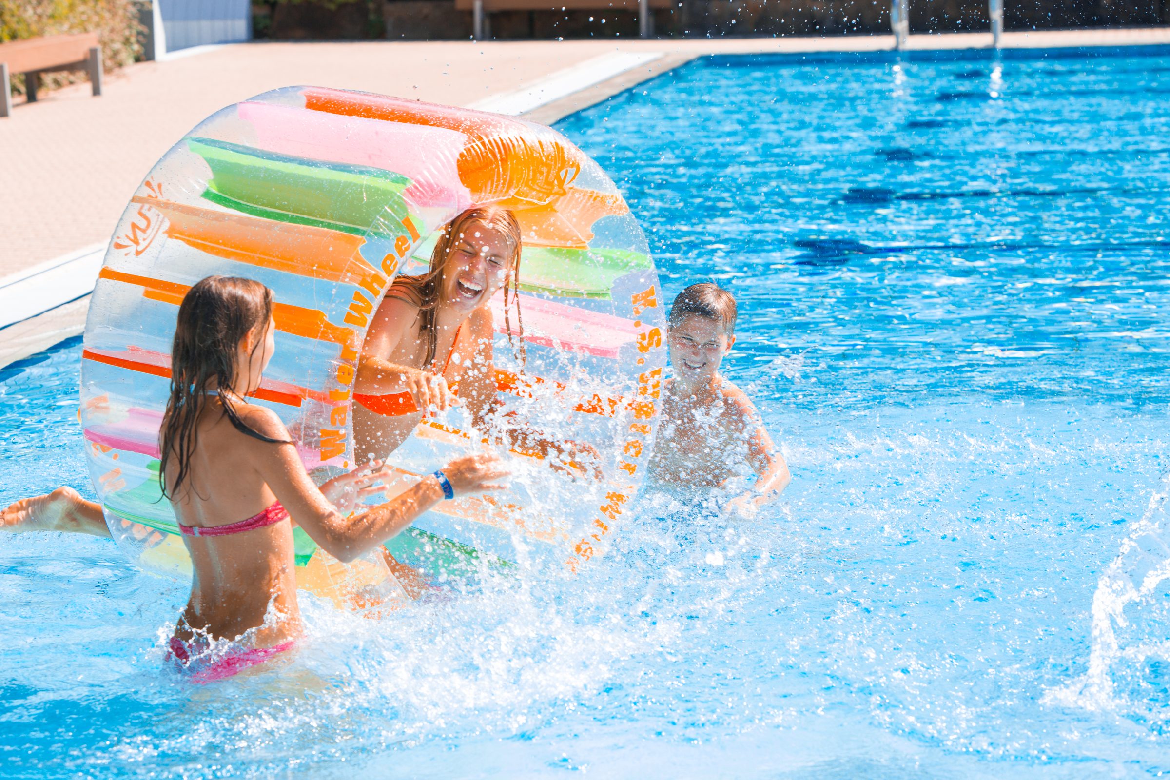 Kinder spielen lachend mit einer bunten aufblasbaren Wasserwalze im Becken eines Freibads der Stadtwerke Heilbronn