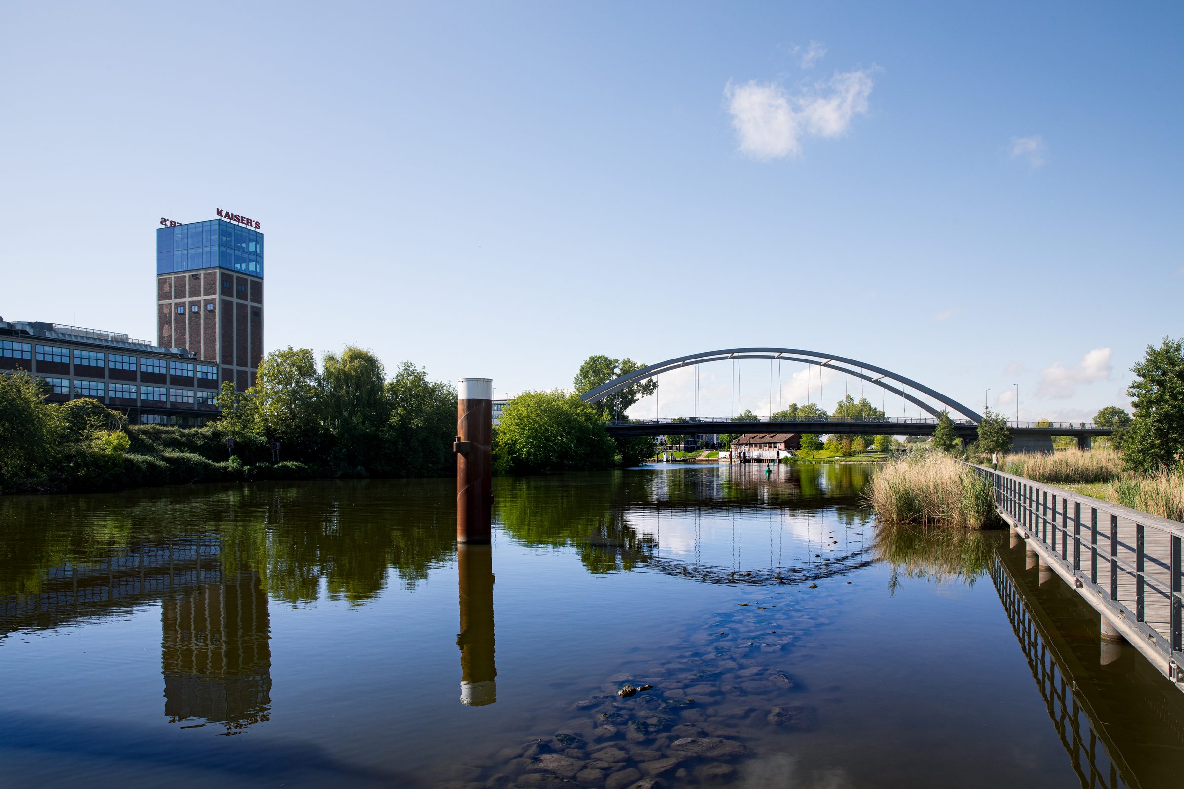 Der Neckar in Heilbronn mit Spiegelungen im Wasser, im Hintergrund eine Bogenbrücke und ein Hochhaus
