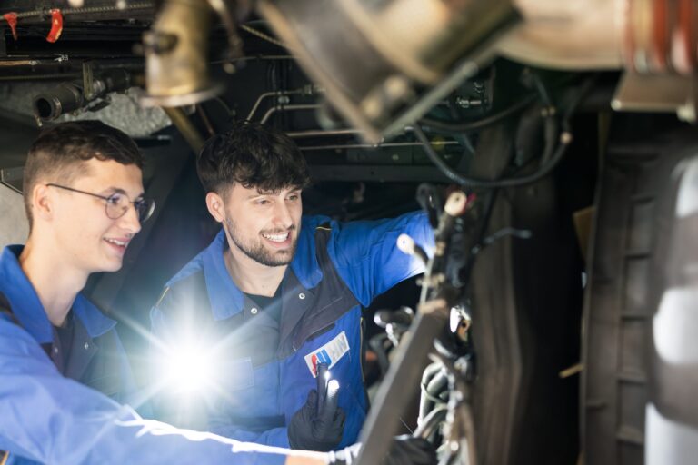 Zwei Auszubildende in blauer Arbeitskleidung prüfen mit einer Taschenlampe die Technik unter einem Bus der Stadtwerke Heilbronn