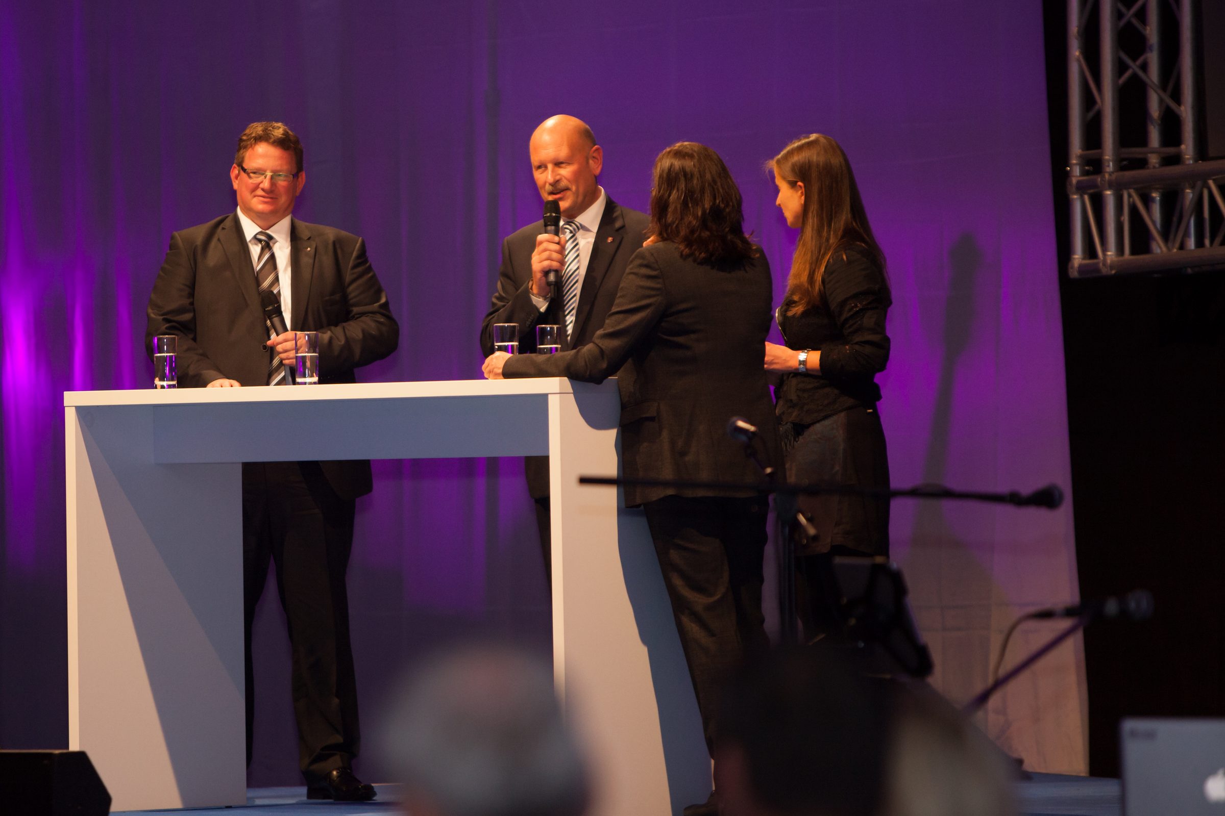 Vier Personen stehen an einem Stehtisch mit Mikrofon auf der Bühne beim Firmenjubiläum von Weber Hydraulik