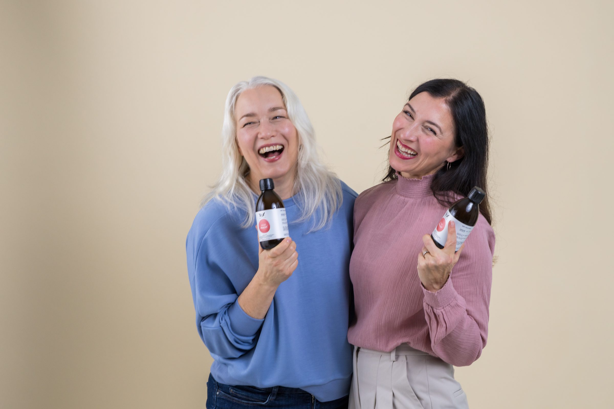 Zwei lachende Frauen halten kleine Produktflaschen von XbyX in die Kamera