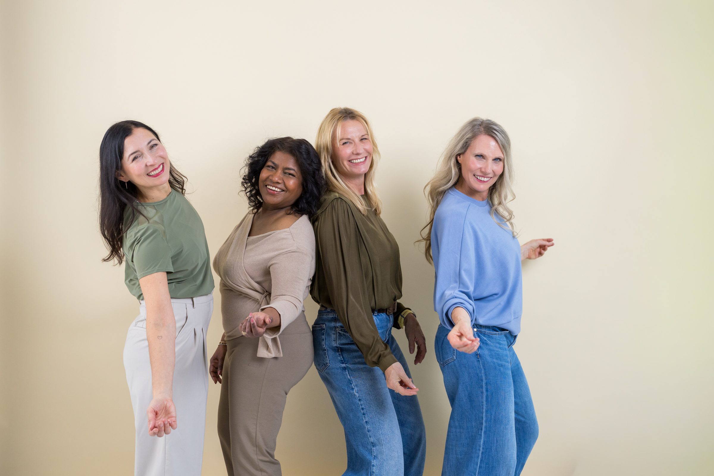 Vier lachende Frauen in Jeans und gedeckten Farben posieren gemeinsam vor einer hellen Wand, Markenshooting für XbyX
