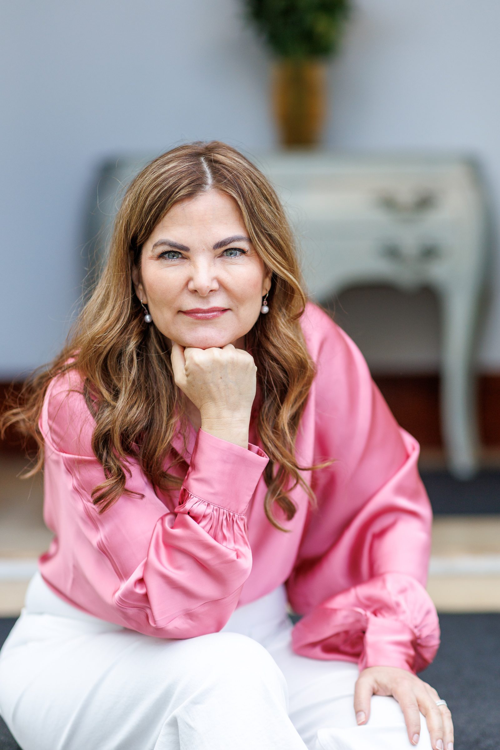 Porträt von Sheila de Liz in rosa Seidenbluse, das Kinn auf die Hand gestützt