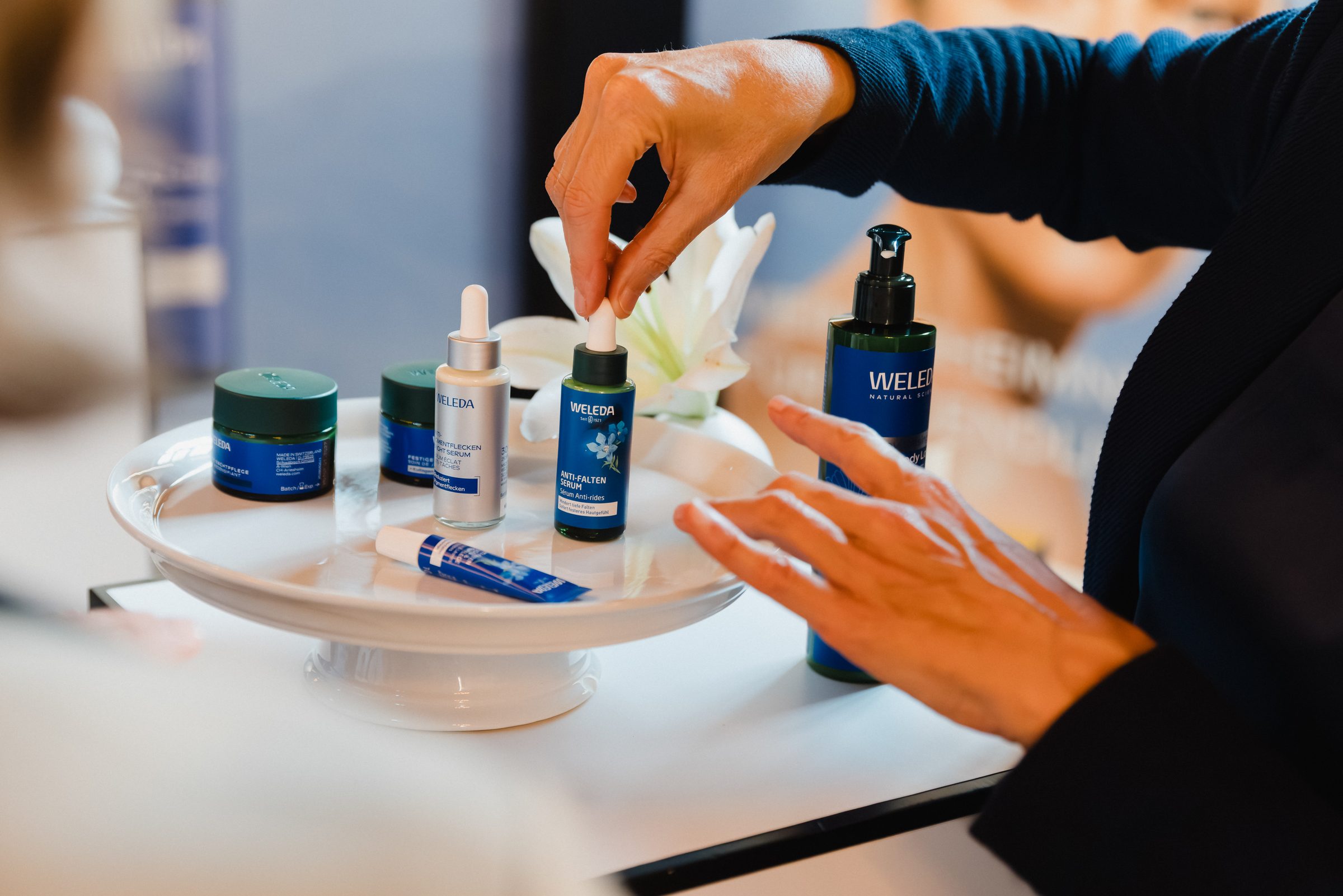 Hände greifen nach Pflegeprodukten auf einer weißen Etagere beim Pro Age Event von XbyX