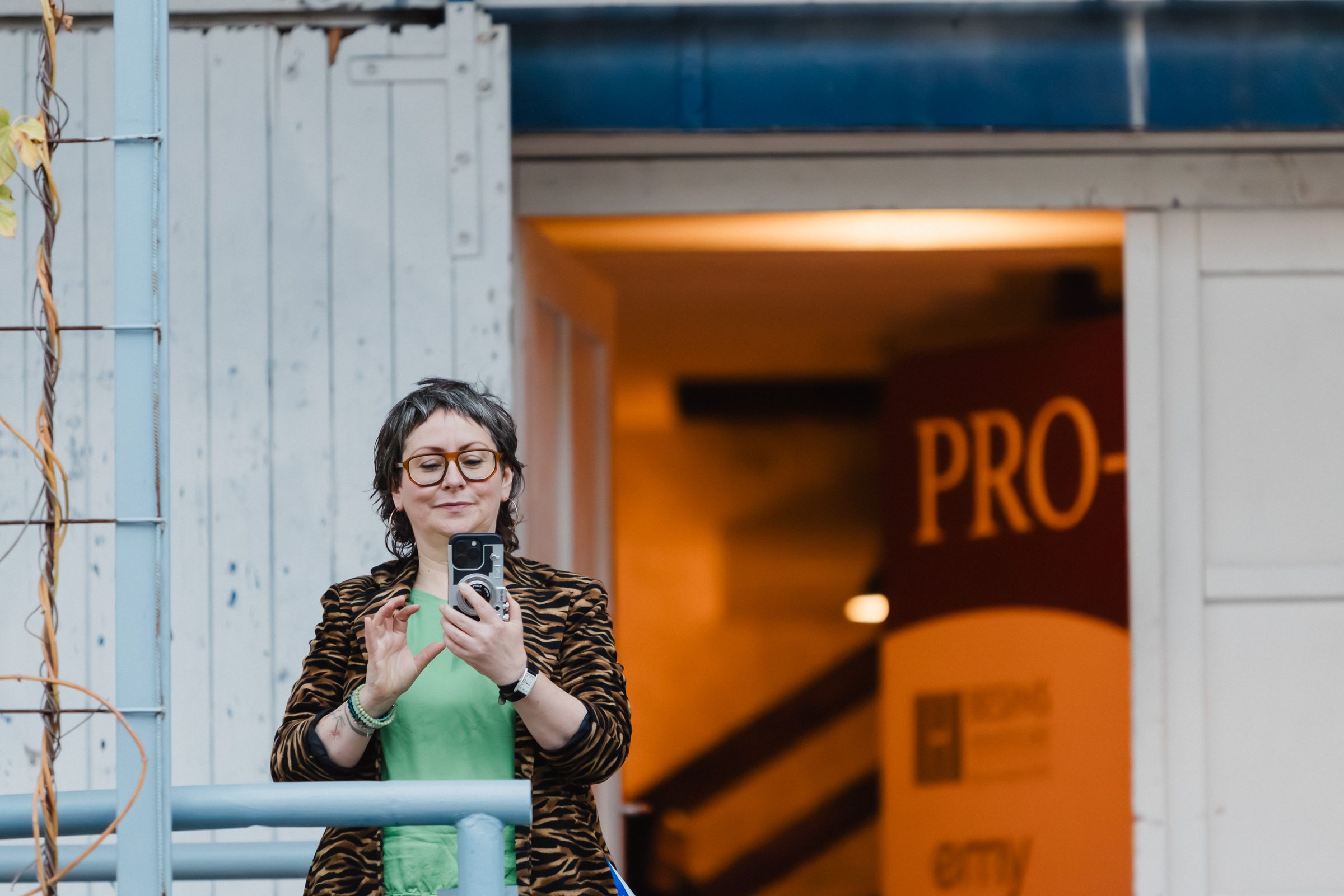 Frau im gemusterten Mantel fotografiert mit dem Smartphone vor dem Eingang zum Pro Age Event von XbyX