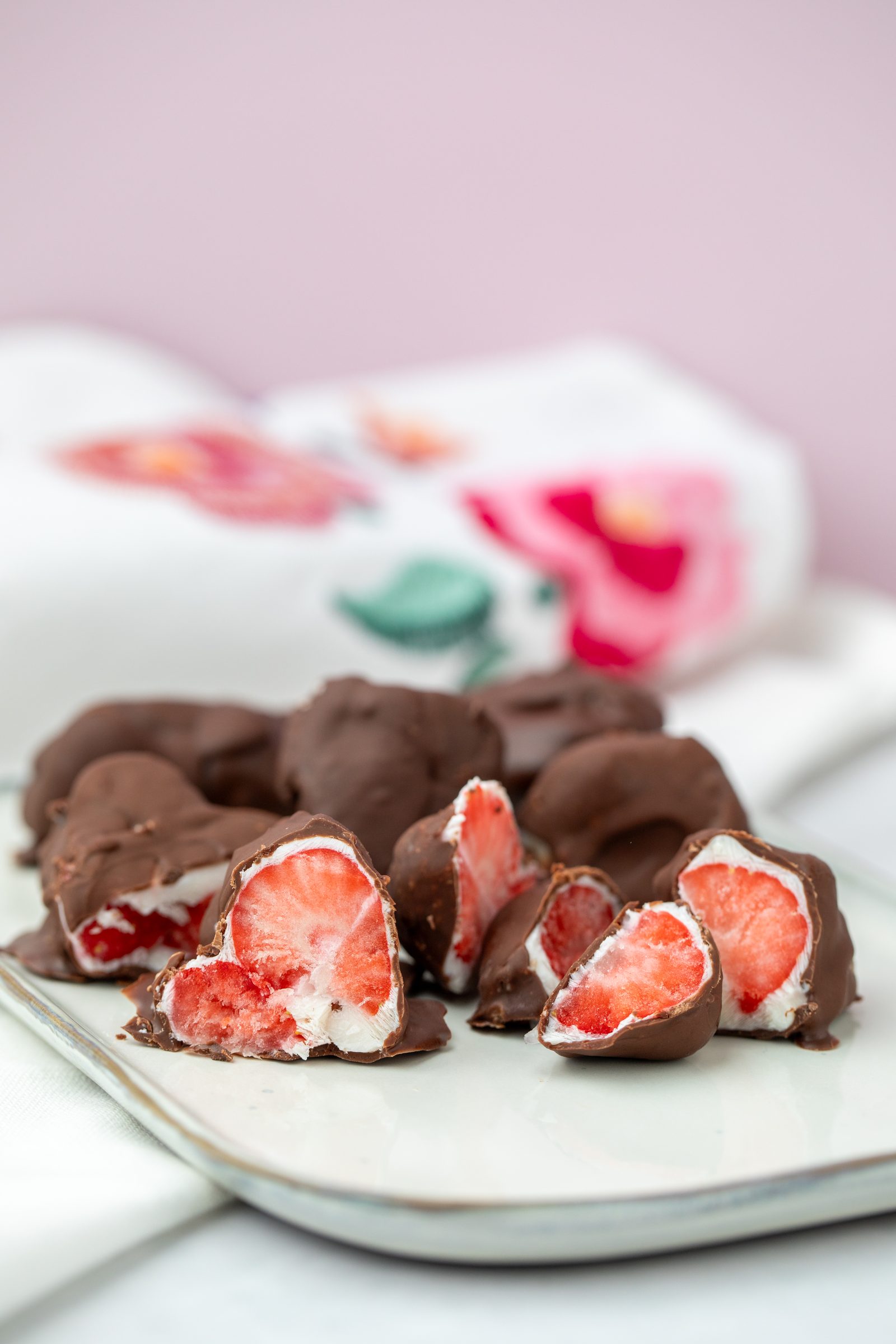 Halbierte Erdbeeren mit Schokoladenüberzug auf einem hellen Teller vor rosa Hintergrund, Rezeptfoto für XbyX