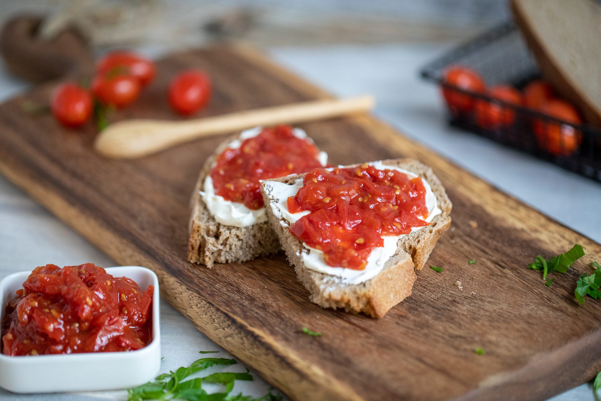 Brotscheiben mit Frischkäse und Tomatenmarmelade auf einem Holzbrett, daneben Kirschtomaten